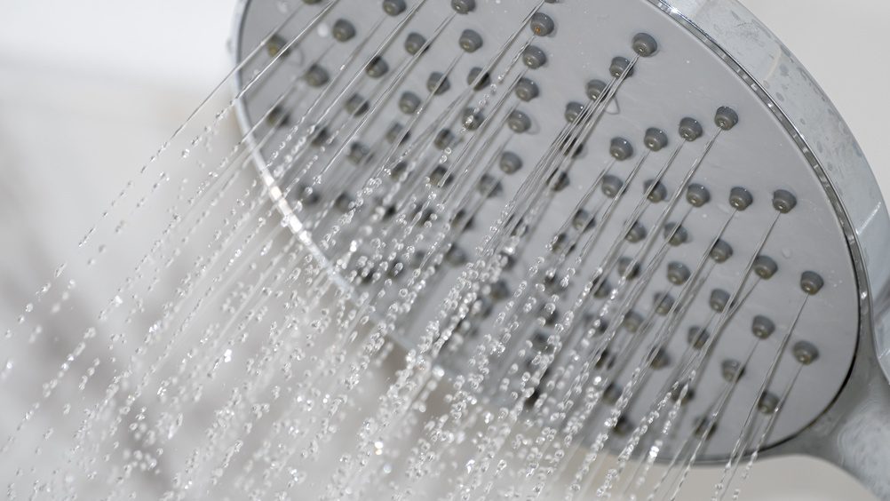 Close-up of a metallic showerhead actively spraying water, showcasing clean design, strong pressure, and detailed nozzle pattern in a bright setting.