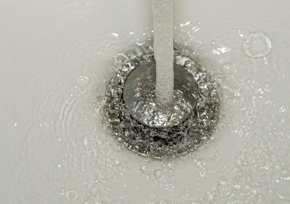 Macro shot of water stream pouring directly onto chrome sink drain plug